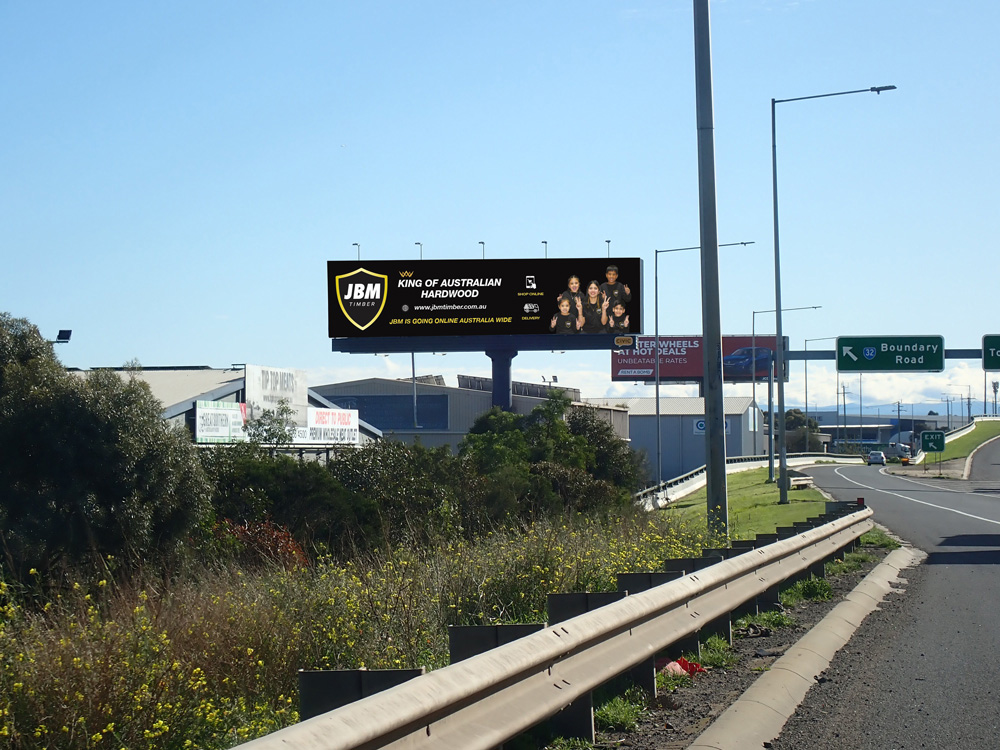  Highway billboard advertising JBM Timber as the "King of Australian Hardwood," with a logo and images of workers